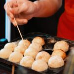 a person holding a stick over a tray of food