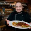 man in black zip up jacket sitting beside table with food