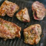 Five pieces of seasoned meat cooking on a grill pan.