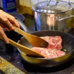 Chef cooking meat in a frying pan