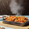a pan filled with food sitting on top of a wooden cutting board