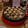 Someone is cooking takoyaki in a takoyaki pan.