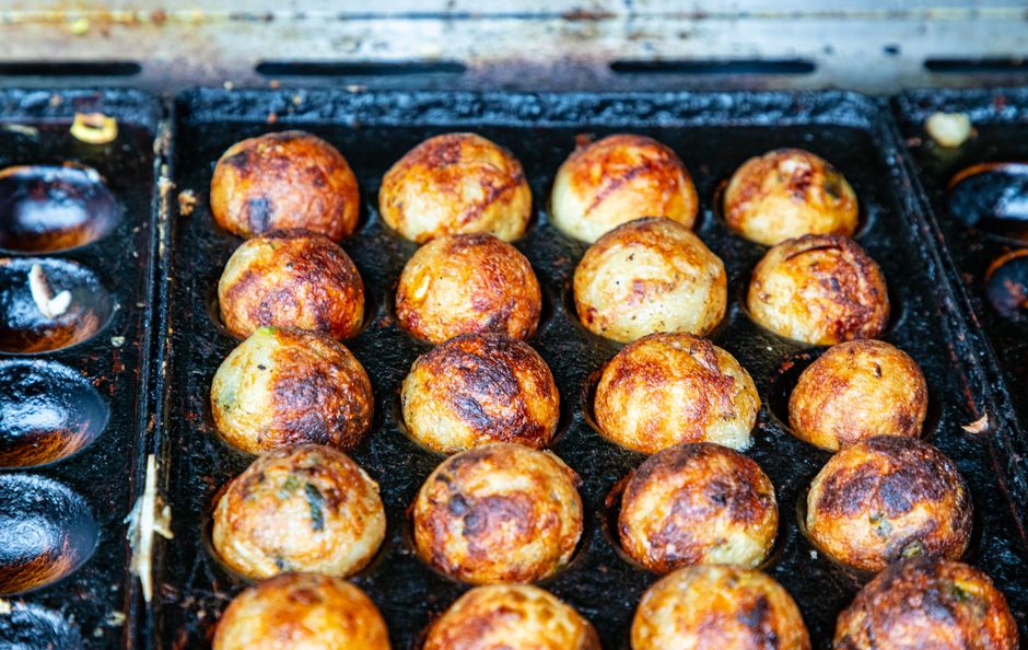 Close-up of takoyaki balls on a traditional grill, showcasing crispy texture and golden brown color.