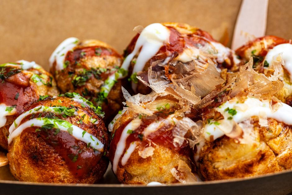 Close-up of freshly prepared takoyaki drizzled with sauce and bonito flakes, a Japanese street food delicacy.