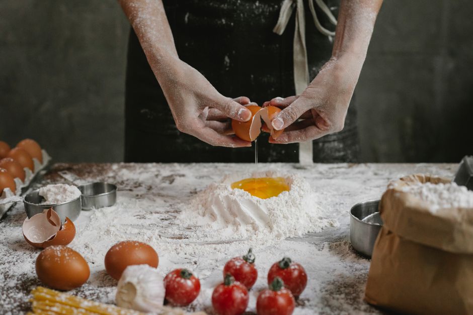 Crop anonymous chef preparing dough for recipe consisting of cherry tomatoes and spaghetti