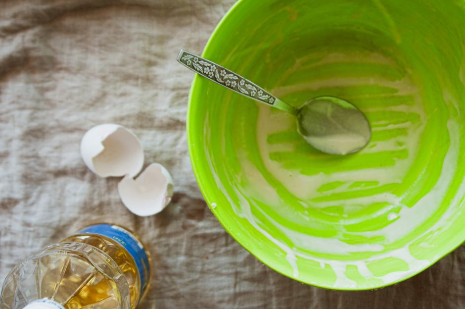 An empty green bowl with spoon, eggshells, and oil on a textured surface.