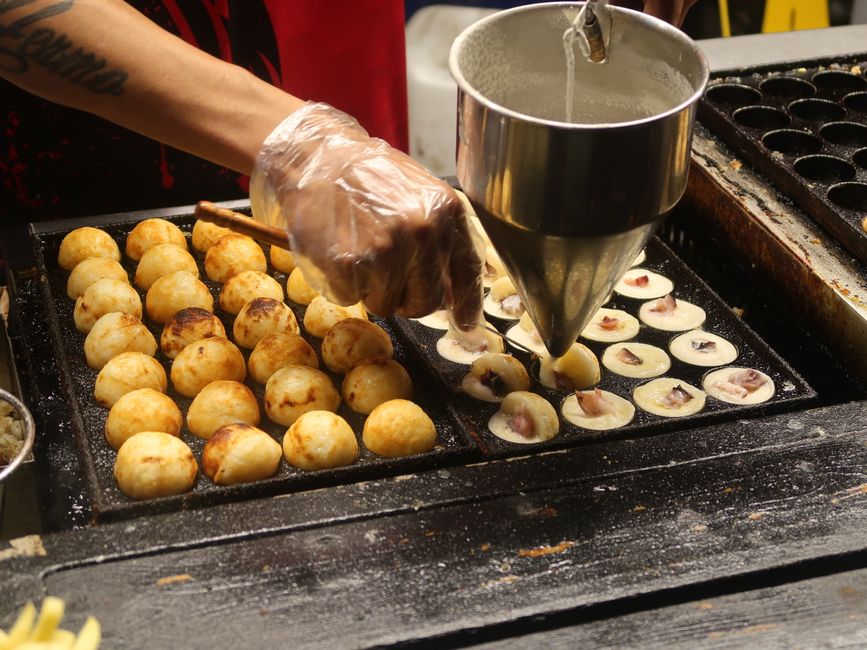 Close-up of a vendor preparing traditional takoyaki in a street market in the Philippines, showcasing the cooking process.