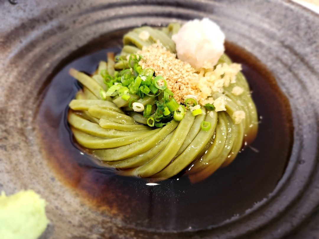 黒い器に盛られた緑色の麺状の料理に薬味を添えた一皿