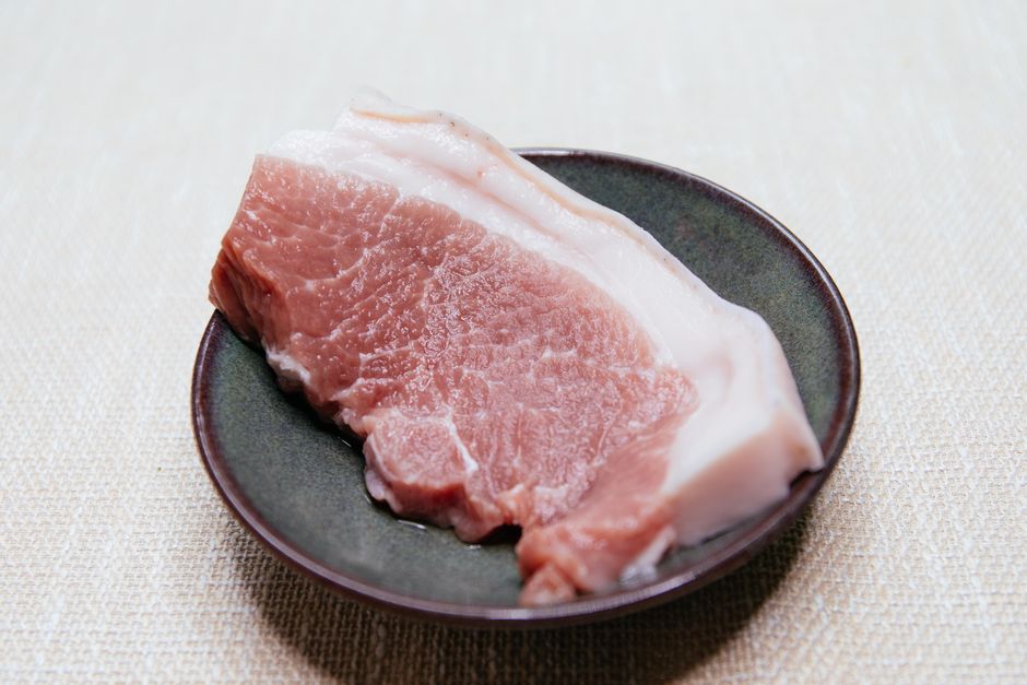 黒い皿に乗った豚バラ肉のスライス、赤身と脂身の層が見える