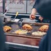 屋台の鉄板でお好み焼きにキャベツと卵をのせて焼いている様子