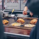 屋台の鉄板でお好み焼きにキャベツと卵をのせて焼いている様子