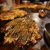 鉄板の上でソースとマヨネーズをかけて焼き上げたお好み焼き