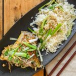 白身魚の切り身を長ねぎと香味野菜と一緒に蒸した皿
