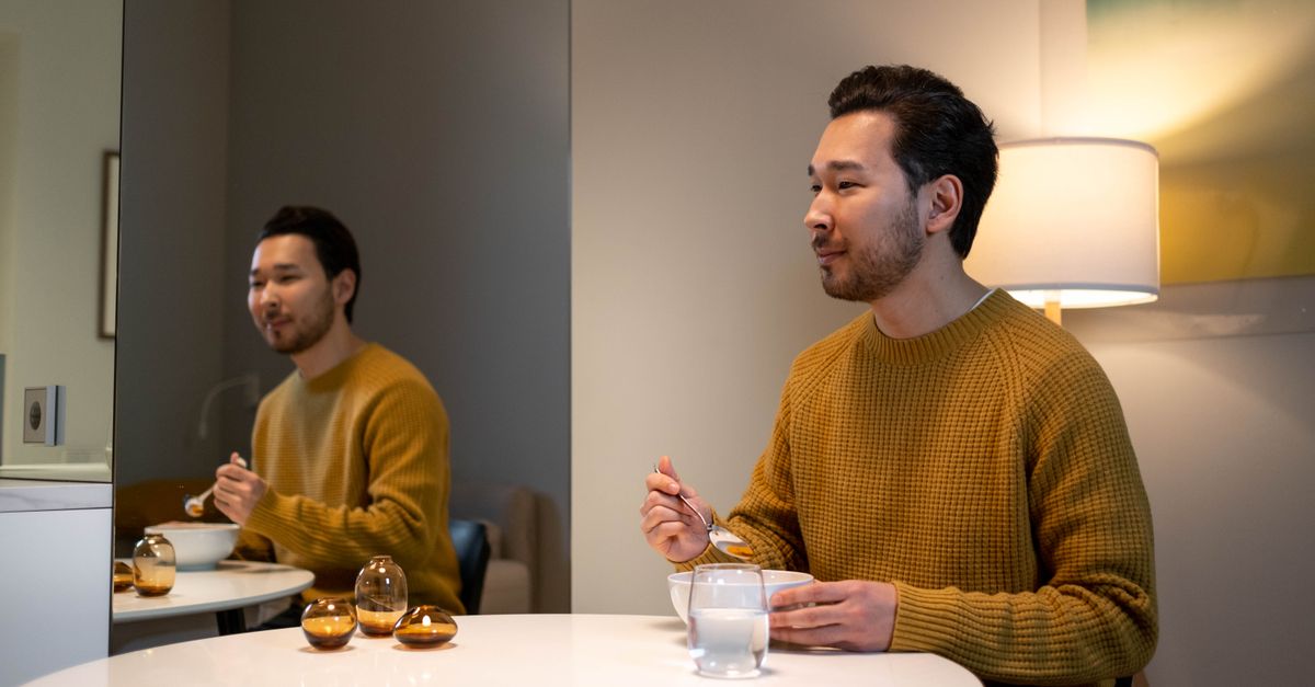 丸いテーブルで一人で食事をする男性、鏡に姿が映っている