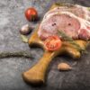 まな板に乗った豚肉のブロックとローズマリー、トマト、にんにくなどの香味野菜