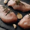 黒いまな板に並んだ鶏むね肉とローズマリー、にんにくの香味野菜