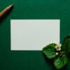 緑の背景に置かれた白紙のカードとペン、いちごの花