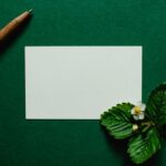 緑の背景に置かれた白紙のカードとペン、いちごの花