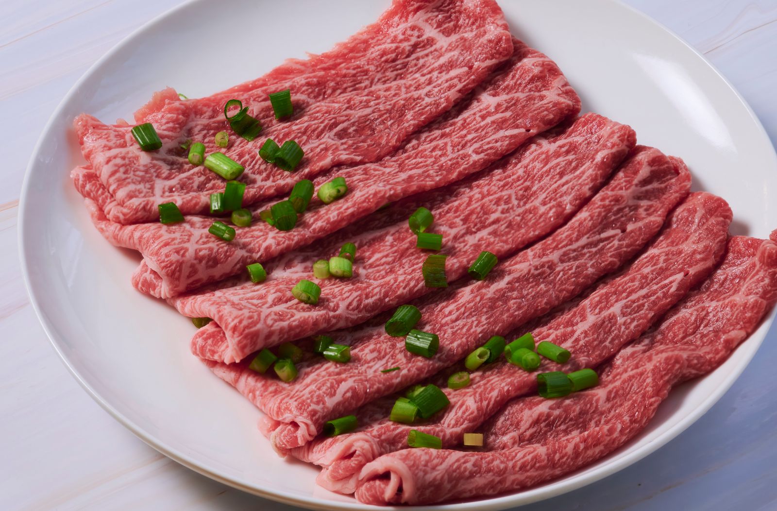 白い皿に盛り付けた霜降り牛肉の薄切りとねぎの薬味