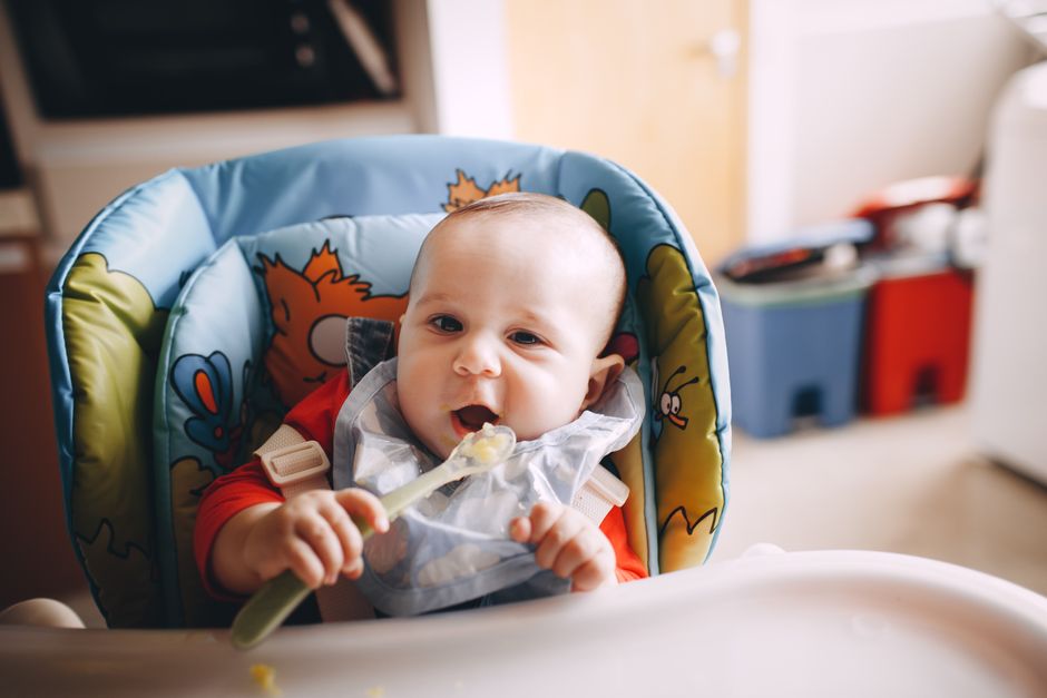 ベビーチェアに座った赤ちゃんが自分でスプーンを持って離乳食を食べている様子