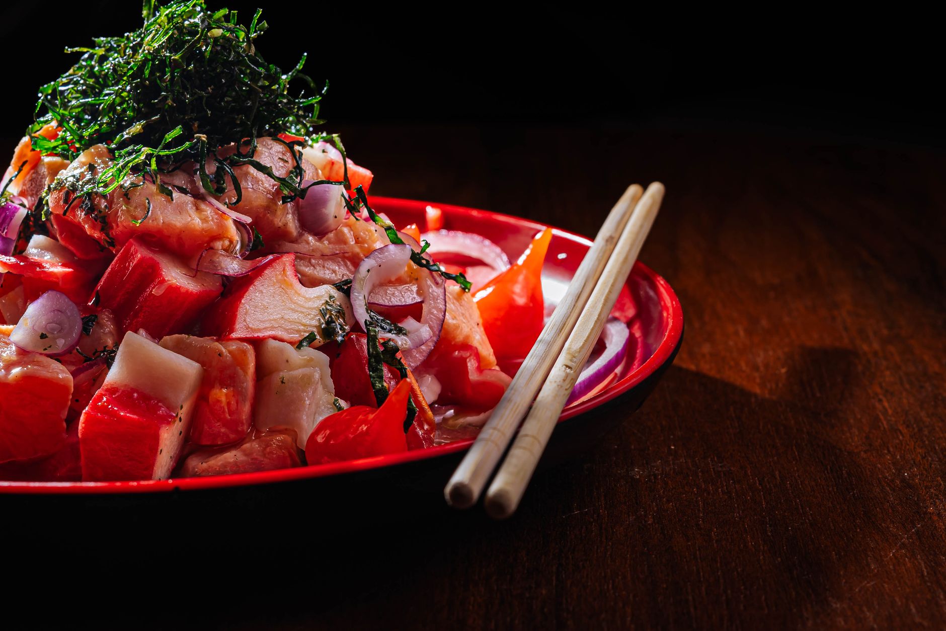 赤い皿に盛られた魚介の和え物に刻み海苔をのせた料理と箸