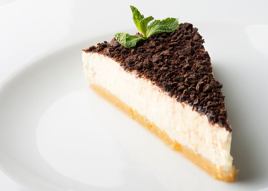 白い背景に置かれた、チョコレートとミントをのせた白いチーズケーキ