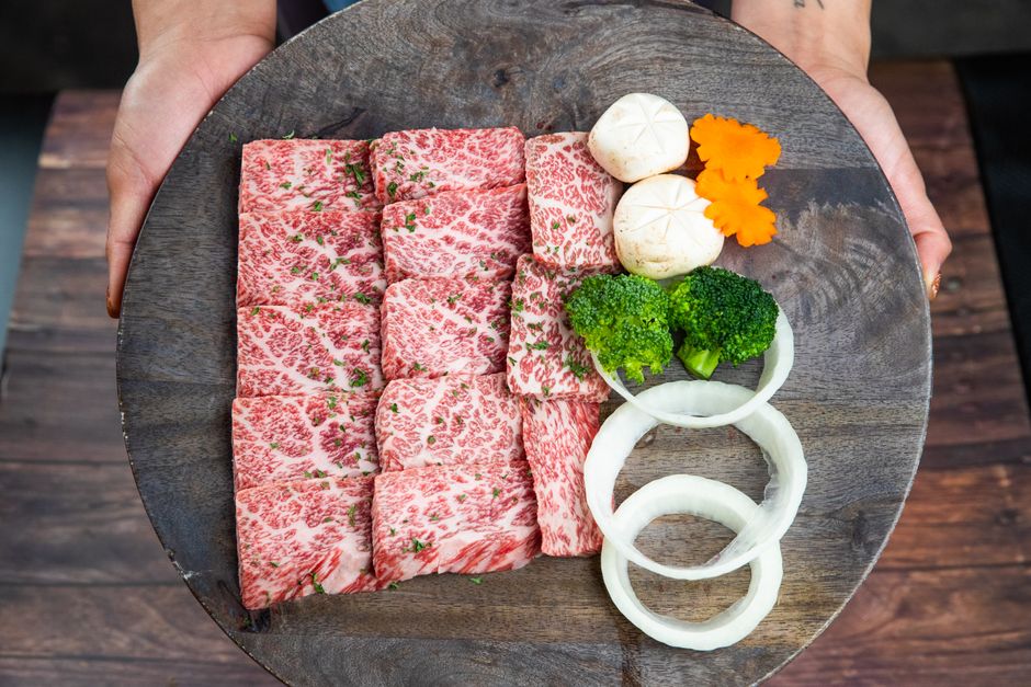 丸い木の板に並べた霜降り牛肉と野菜