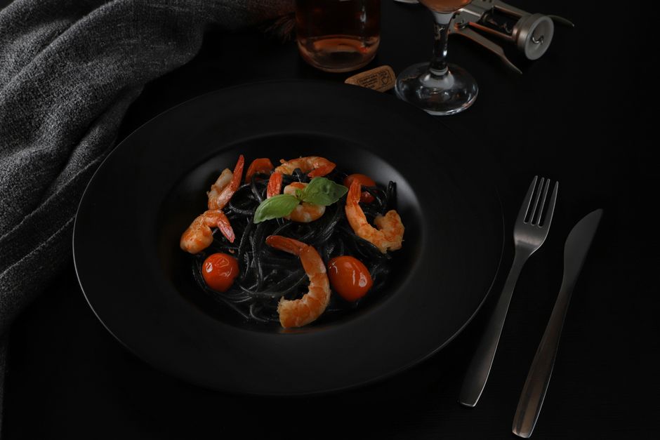 黒い皿に盛ったえびとトマトのいか墨パスタ