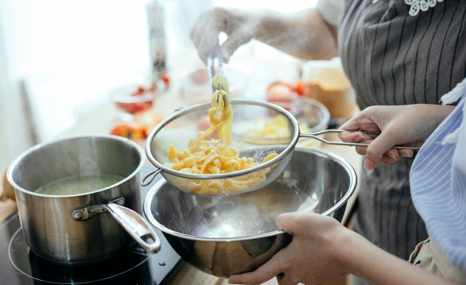 ざるとボウルを使い、茹で上がった麺を鍋からすくい上げている様子