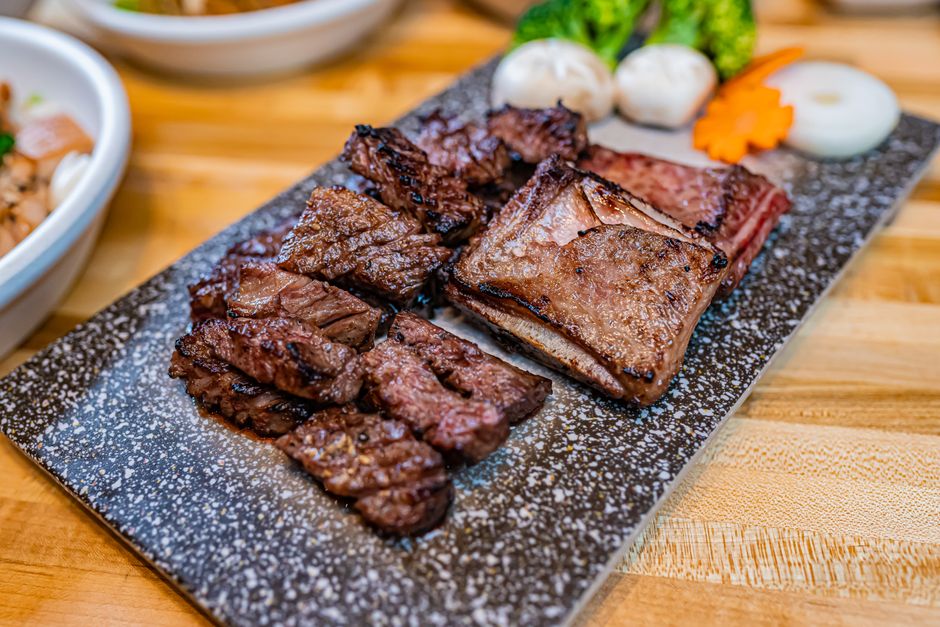 黒い石板に盛られた焼いた牛肉と点心、野菜の付け合わせ