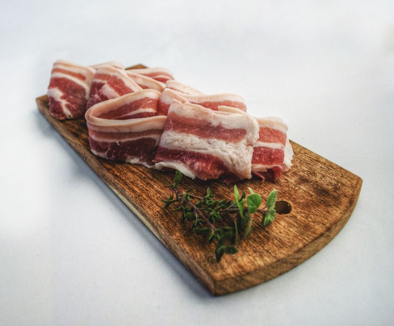 木製のまな板に並べた豚バラ肉とハーブ