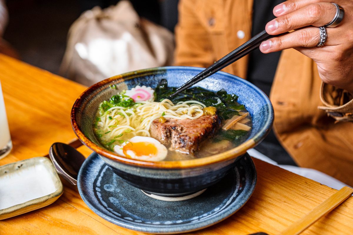 箸で麺を持ち上げる塩ラーメンの写真。青い器に澄んだスープが見える