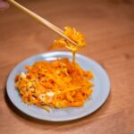 細切りにんじんと卵を炒めた料理を箸でつまむ様子