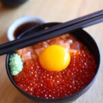 いくらと卵黄をのせた海鮮丼を箸とともにクローズアップで撮影した写真