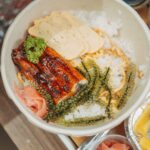白い茶碗によそったご飯の上に、たれと香ばしい焼き目のついた鰻の蒲焼きがのり、みじん切りのパセリと錦糸卵、とびことガリが添えられている