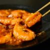 箸でつまんだ照りのある赤いソースのえびチリ