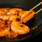 箸でつまんだ照りのある赤いソースのえびチリ
