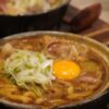 土鍋で煮込んだ麺料理に半熟卵とねぎをのせた一皿