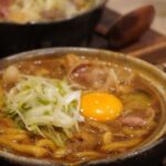 土鍋で煮込んだ麺料理に半熟卵とねぎをのせた一皿