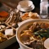 湯気の立つ鍋料理と木箱の具材が並んだテーブル