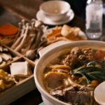 湯気の立つ鍋料理と木箱の具材が並んだテーブル