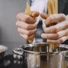 両手で乾燥パスタをつかみ、湯気の立つ鍋に入れようとしている様子