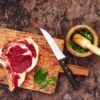木のまな板に置かれた生の牛肉の塊と、包丁やハーブをすりつぶすすり鉢