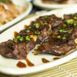 白い皿に盛られた、ネギとタレをかけて焼いた牛肉の一口カット