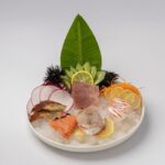 白い背景に盛られた、うにや大根のつまを添えた刺身の盛り合わせ