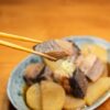 大根と一緒に甘辛く煮た魚の切り身を箸でつまむ様子
