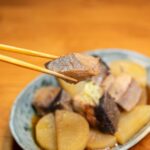 大根と一緒に甘辛く煮た魚の切り身を箸でつまむ様子