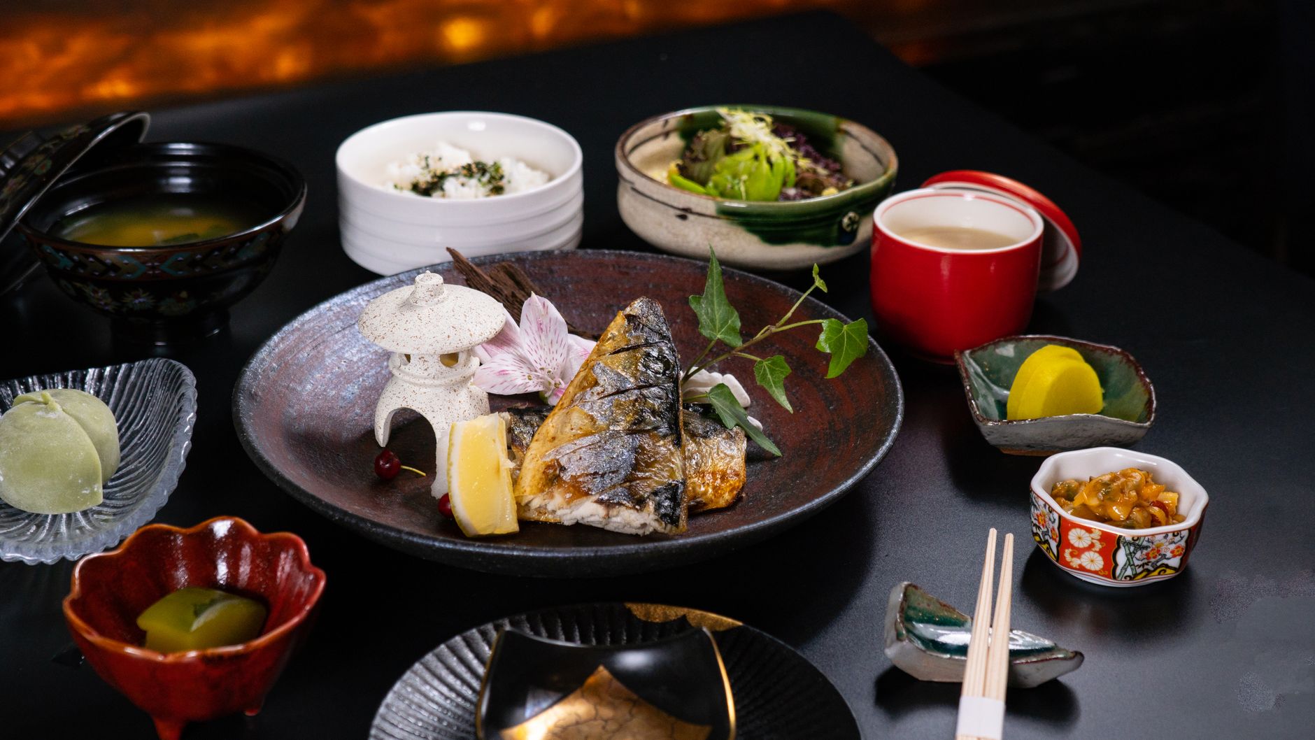 黒い器に盛られた焼き魚を中心に、ご飯や味噌汁、小鉢がいくつも並ぶ和食の会席膳