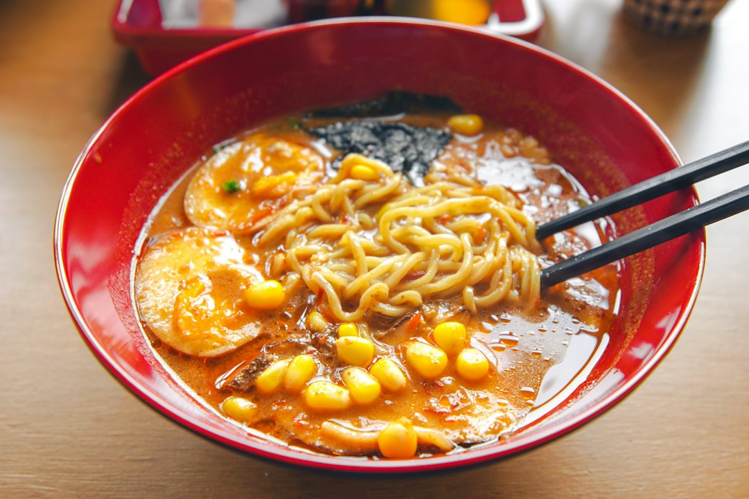 赤い器に盛った味噌ラーメンとコーン、半熟卵