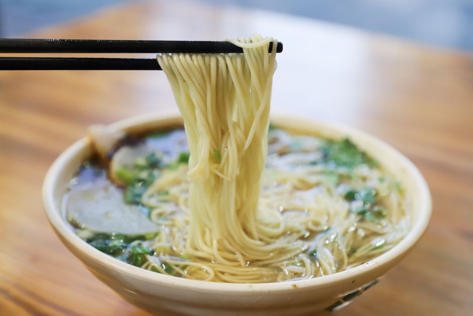 箸で持ち上げた麺と、青菜の入ったスープのラーメン